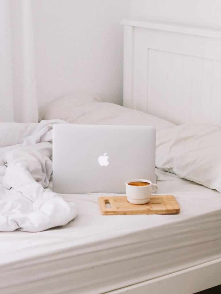 Laptop on a set of white sheets with a coffee next to it 