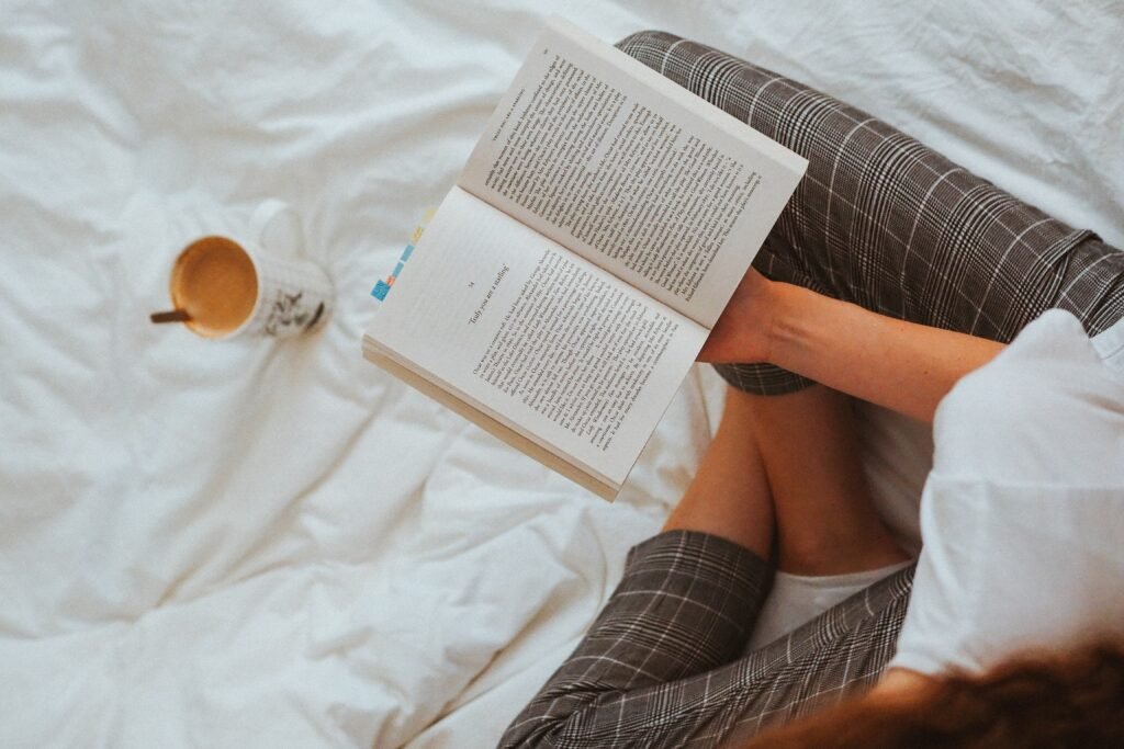 Girl reading a book in bed with a coffee next to her 