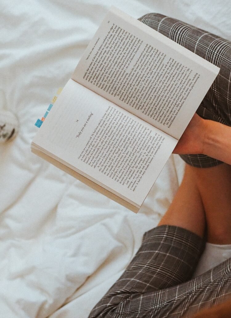 Girl reading a book in bed with a coffee next to her